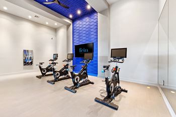 A room with a blue wall and a row of stationary bikes.